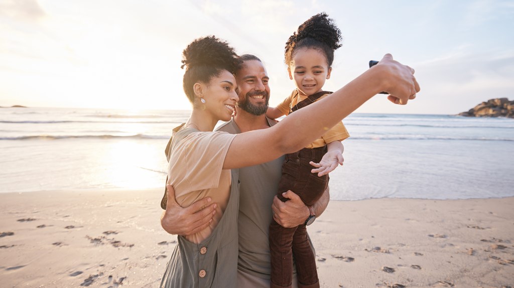 Family of three takes a selfie on the beach.