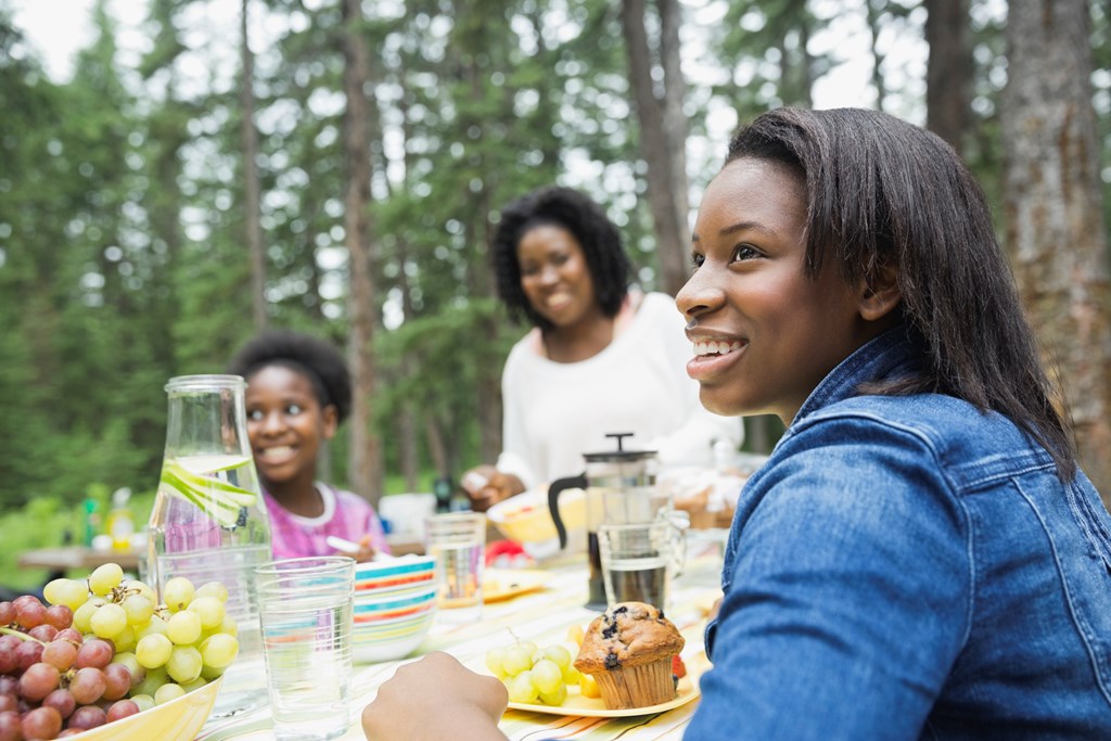 A smiling teenage girl enjoys a meal at a KOA campground with her mother and sister.