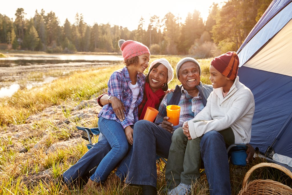 Grandparents camp in a tent with their two grandchildren in the fall season.