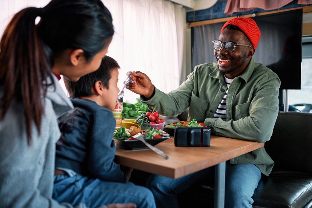 A happy young family of three has dinner in their RV.