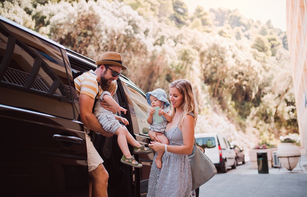 A young family with two toddler children getting out of a car on summer holiday.