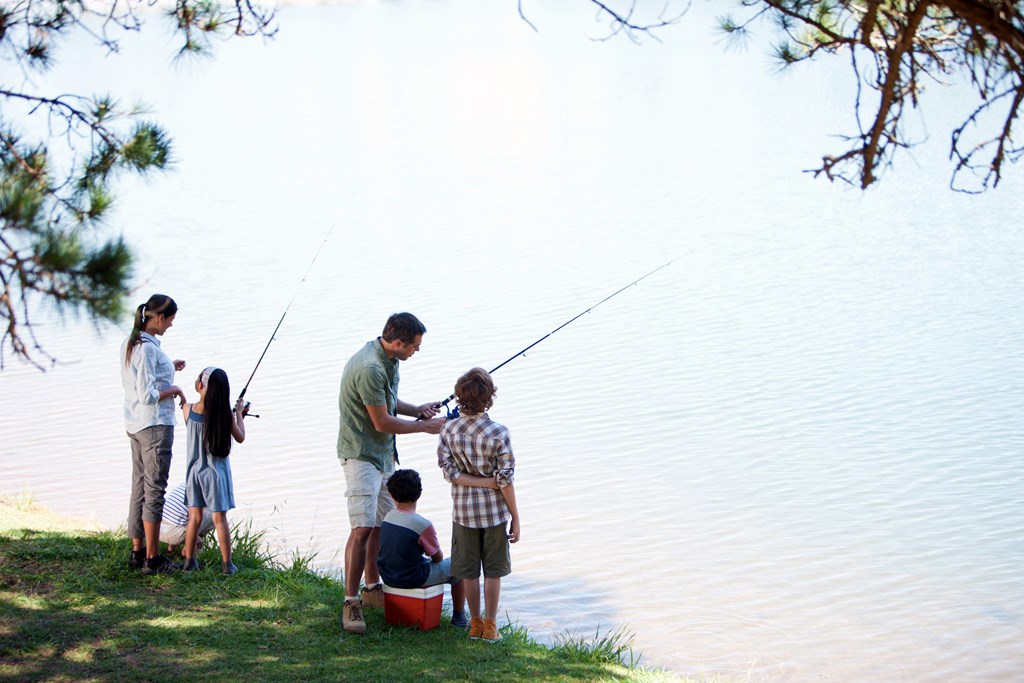 A family of five fishing in the shade on a lake.