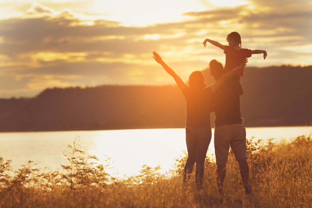 Silhouette of a family of three in the sunshine by a lake.