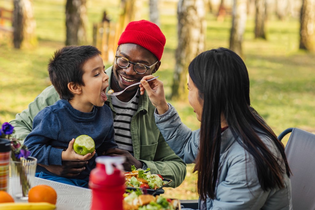 A young mother and father feed their young son on a camping trip.