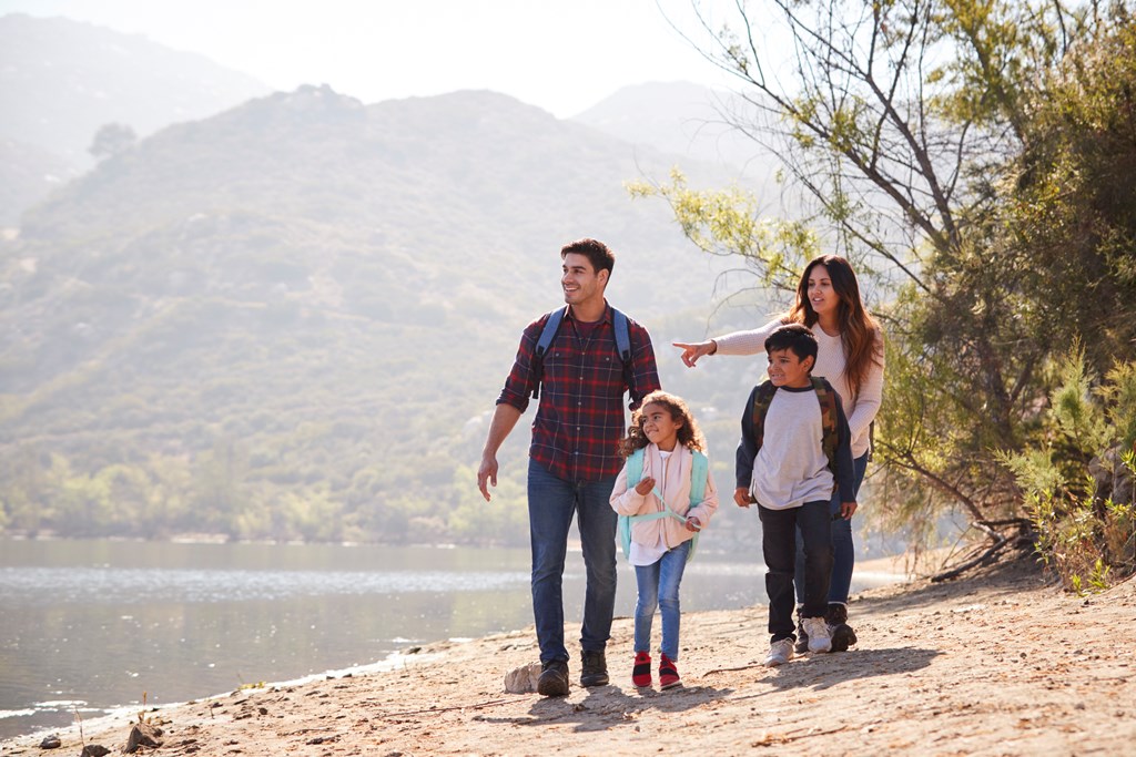 A family of four takes a hike on a sunny day by a lake.