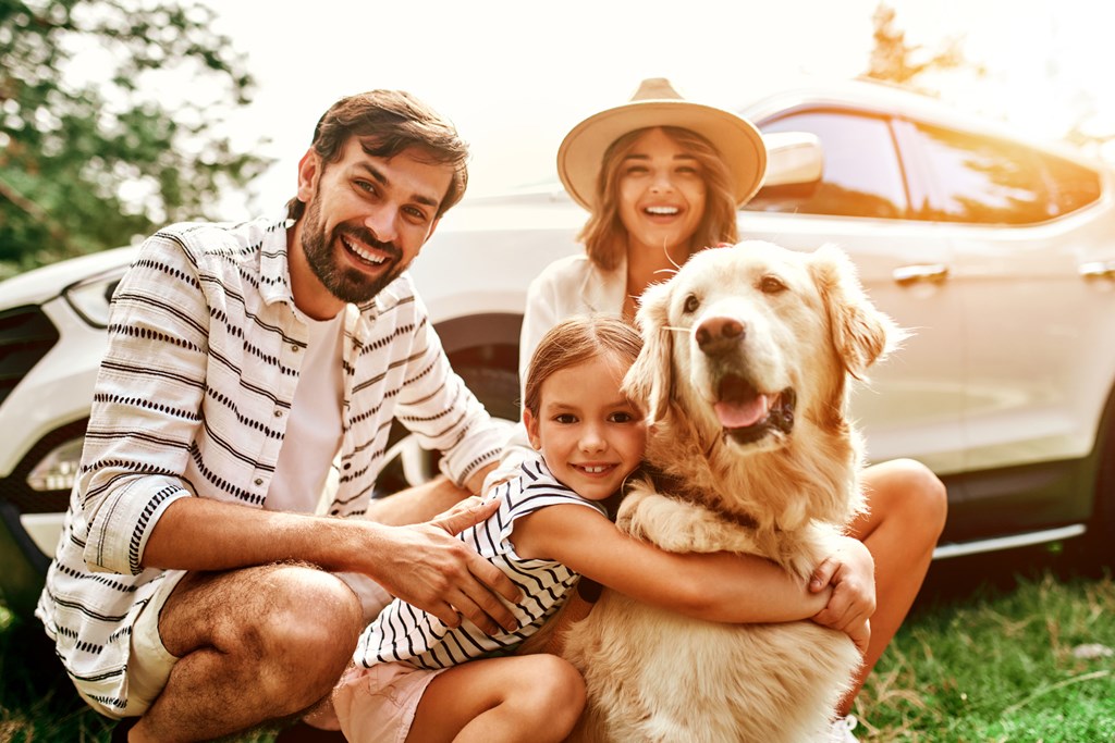 A family poses in front of their car on a sunny day.