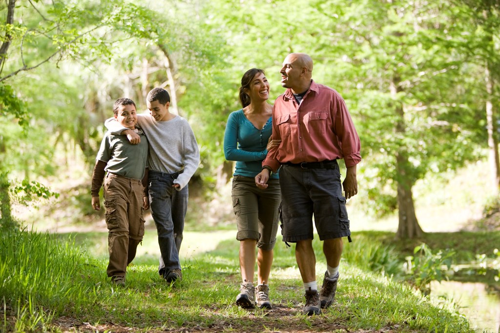 Happy Hispanic family with two boys walking along trail in park.