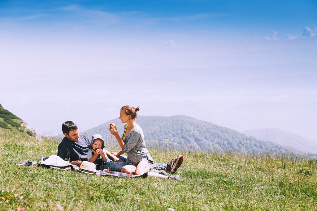 Happy family of three having a picnic in the mountains.