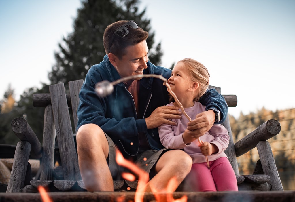 Father roasting marshmallows over a campfire with hi9s young daughter.