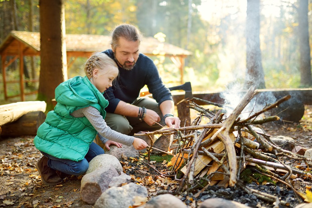 Father teaching young daughter about campfire safety on a camping trip.