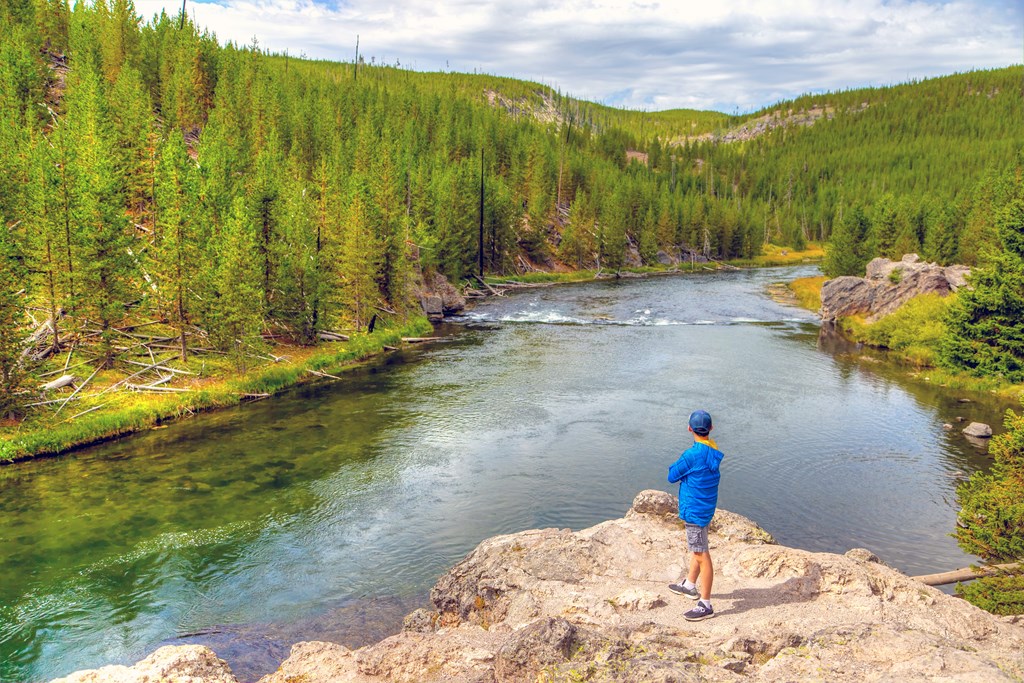 A young visitor looking toward Firehole River in Yellowstone National Park, Wyoming, USA. The river flows through several significant geyser basins in Yellowstone National Park.