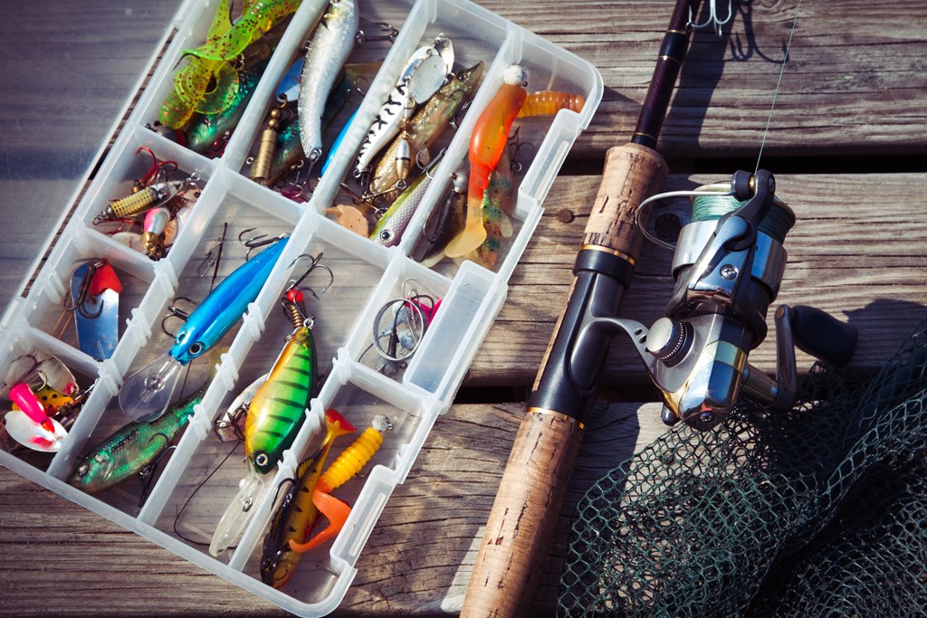 Fishing lures in tackle boxes with spinning rod and net on wooden pier.