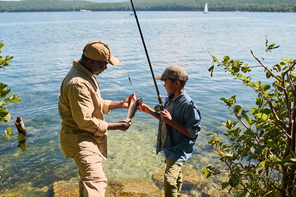 Grandfather and grandson stand by a lake with a fish they caught.