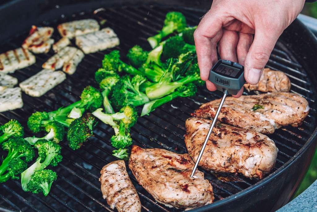 A man measuring the temperature of chicken on the grill thermometer.