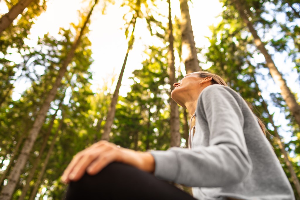 Close up of a woman sitting in a forest and gazing up at the sky.