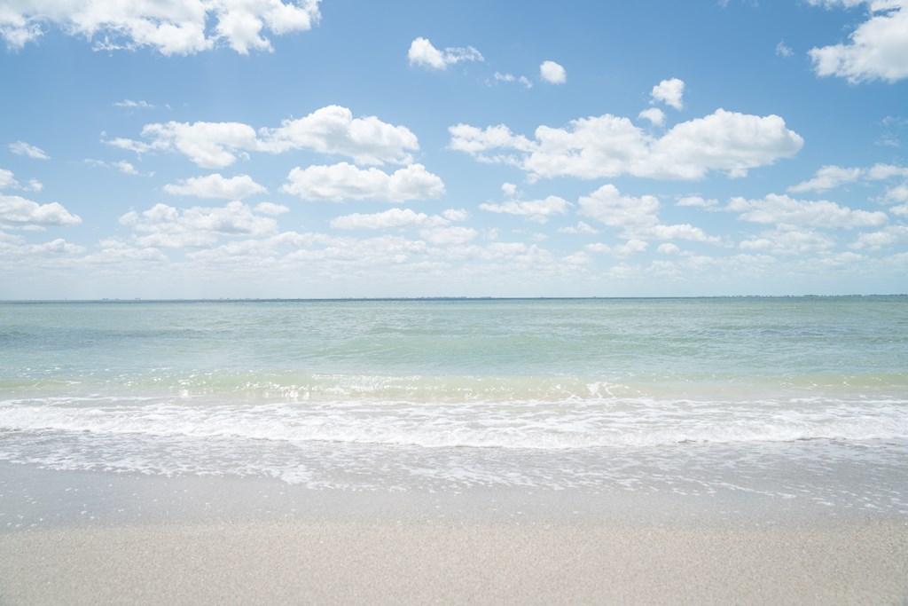 A white sand beach and aqua blue water under a blue sky with fluffy clouds in Fort De Soto, Florida.