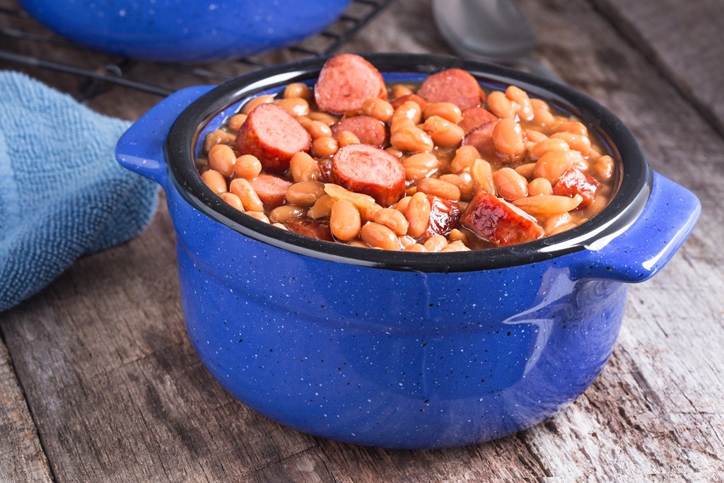 Franks and beans in blue ceramic bowl on a rustic wood table.