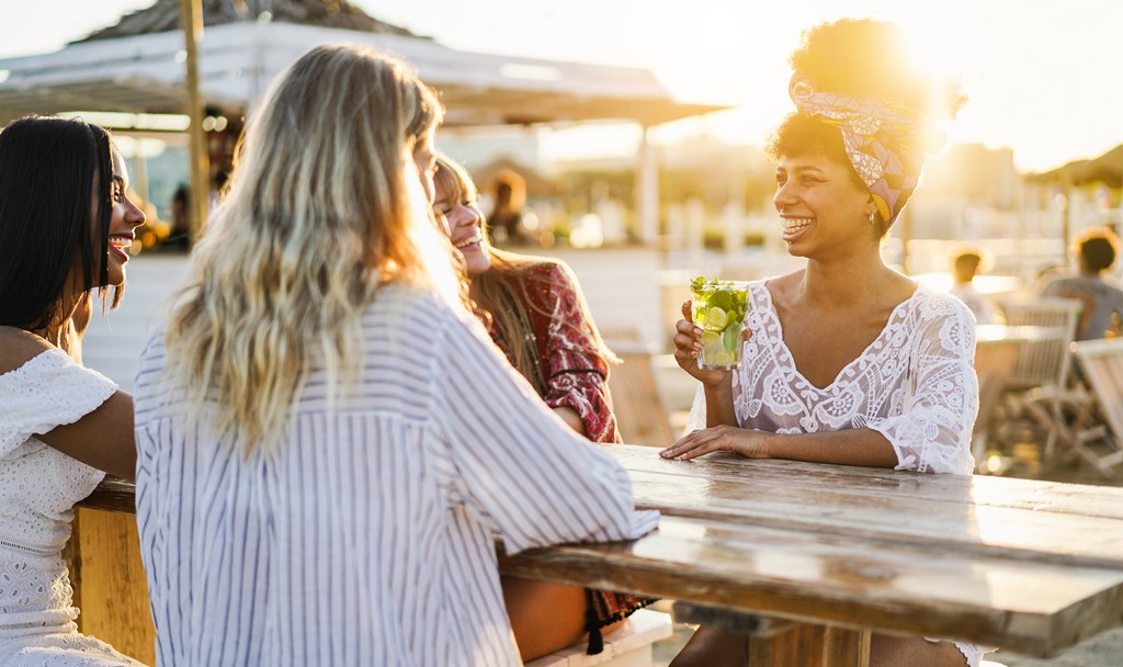 Four female friends share a drink outdoors during sunset.