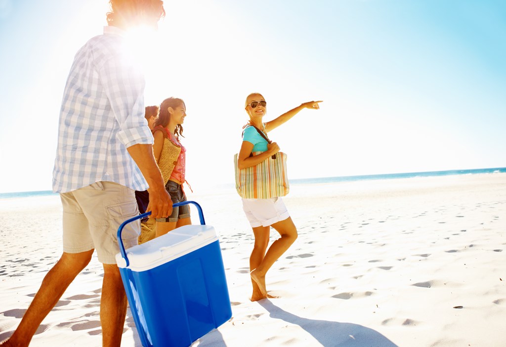 Four young friends walking on the beach carrying a cooler.