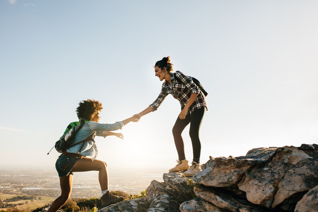 Young woman helping friend to climb up a rock during a hike.