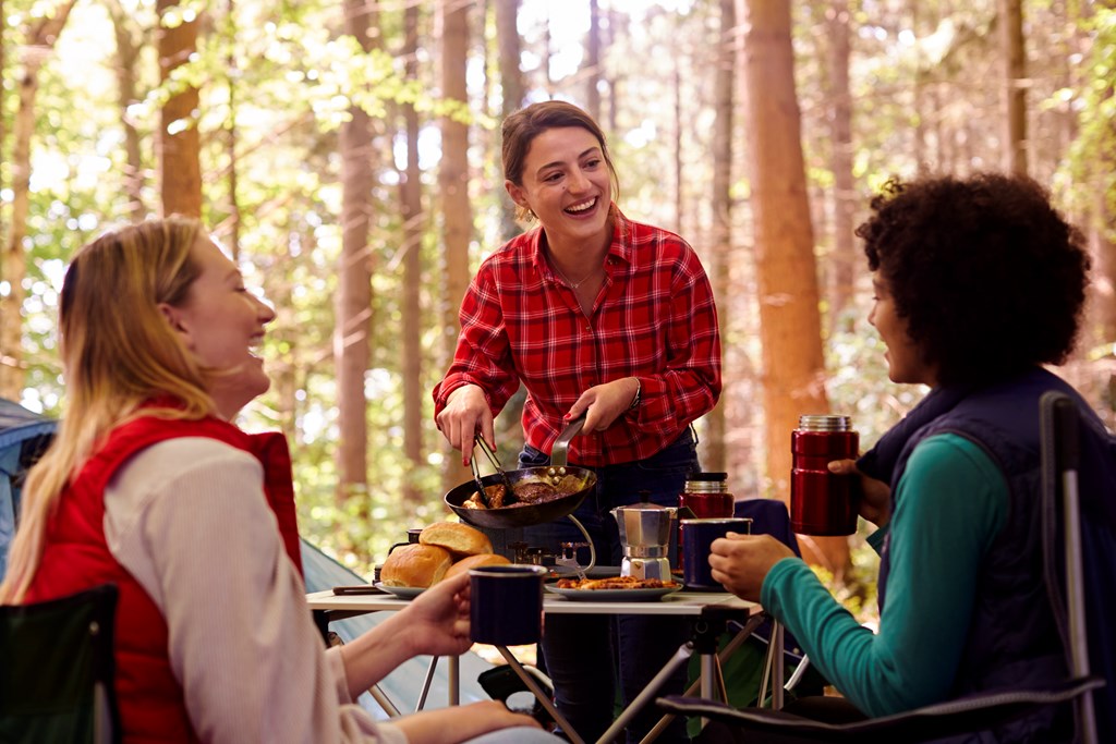 Group of three female friends cooking together on camping trip at KOA.
