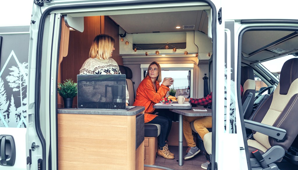 Happy friends having breakfast in a camper van in the morning