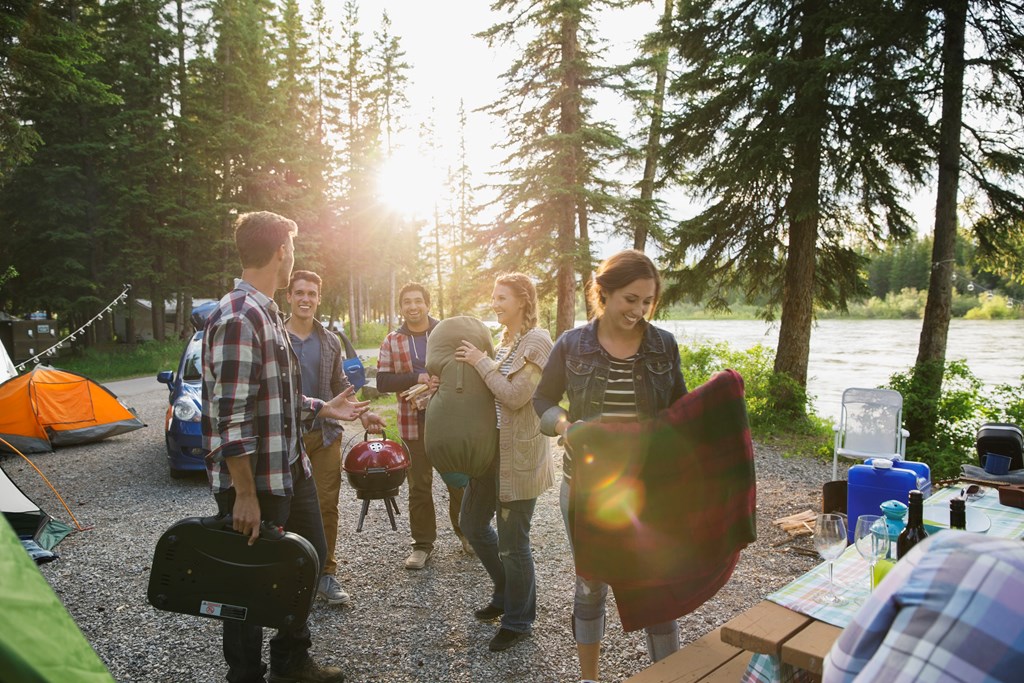 Group of friends packing a campsite by a river.