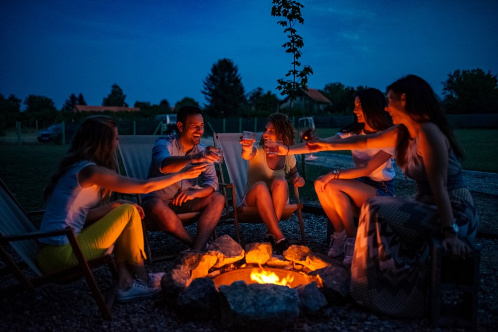 Friends enjoying evening drinks by firepit outdoors.