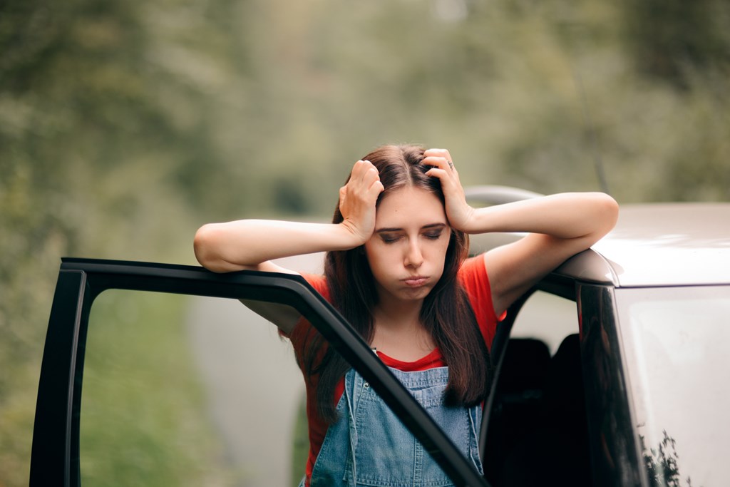 Woman stands near her car frustrated on a road trip.