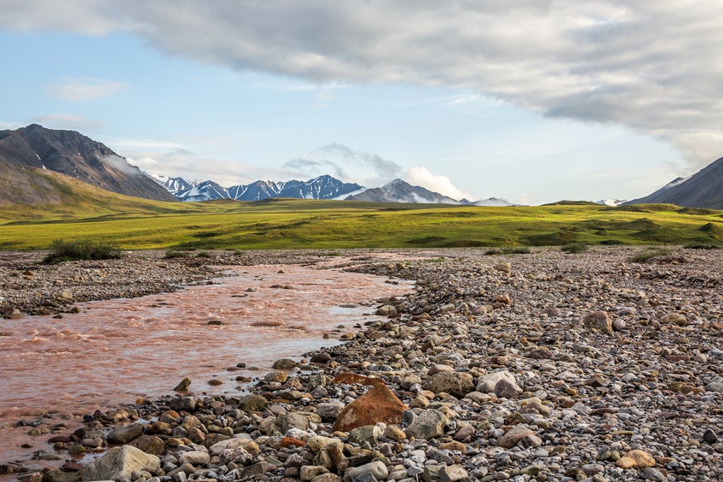 Standing alongside a storm swollen river looking across the arctic tundra with its permafrost palsas towards the remote mountains of the Gates of the arctic National Park. Galbraith Lake, Alaska.