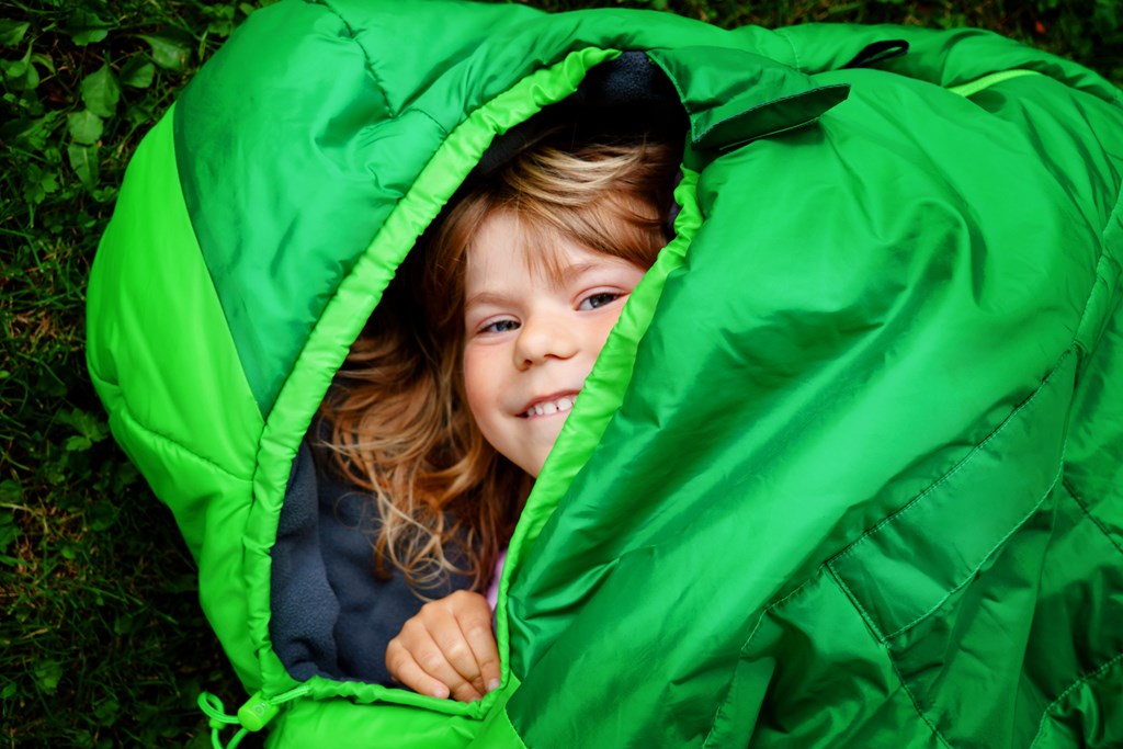 Preschool little girl in sleeping bag camping. 