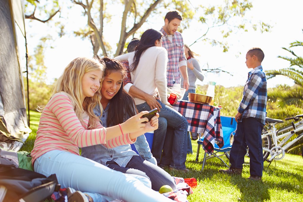 Two teenage girls using a smart phone on a family camping trip.