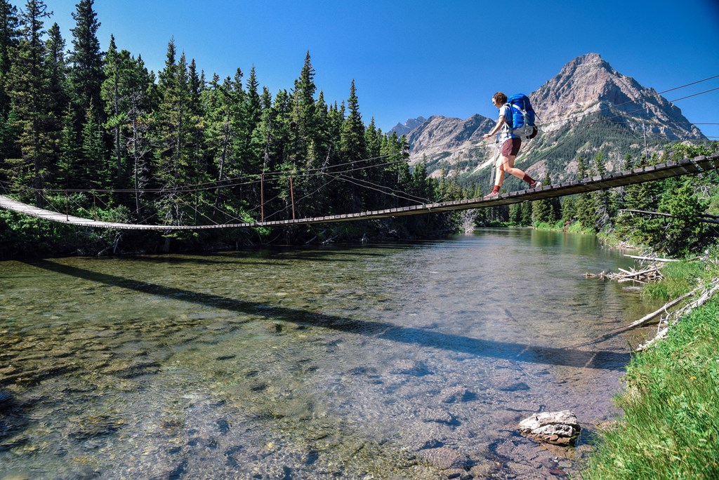 A female hiker crosses a small suspension bridge in Glacier National Park in Montana.