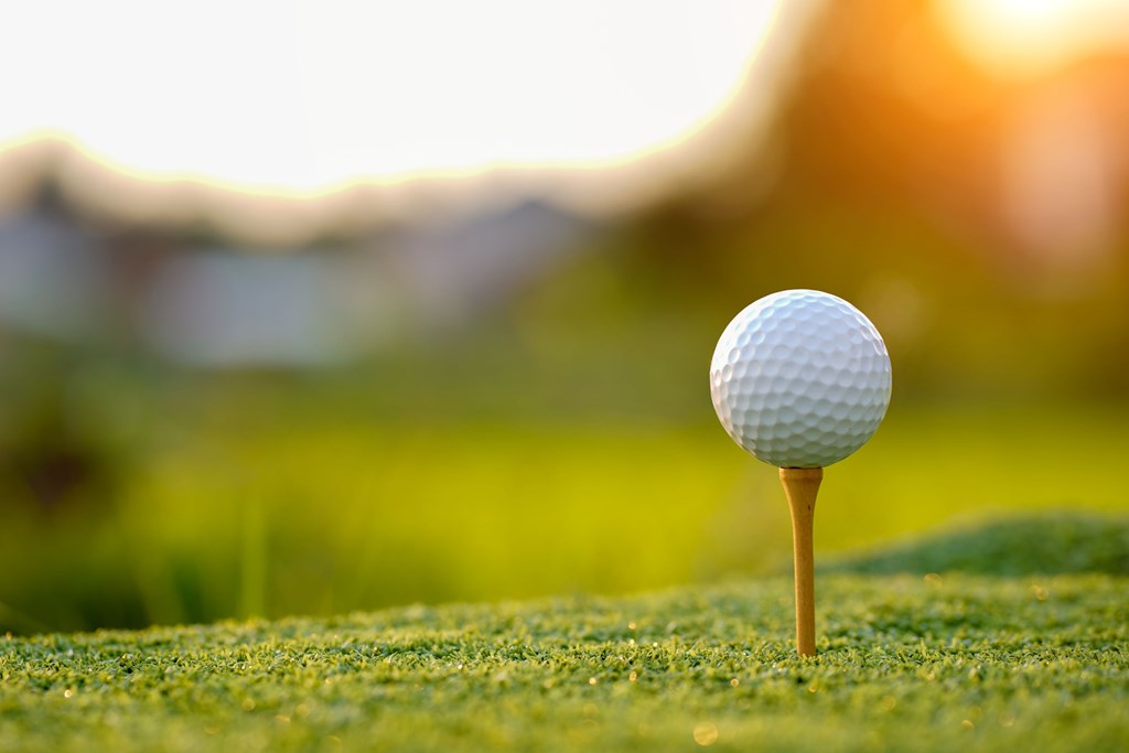 Golf ball on tee in the evening golf course with sunshine background.