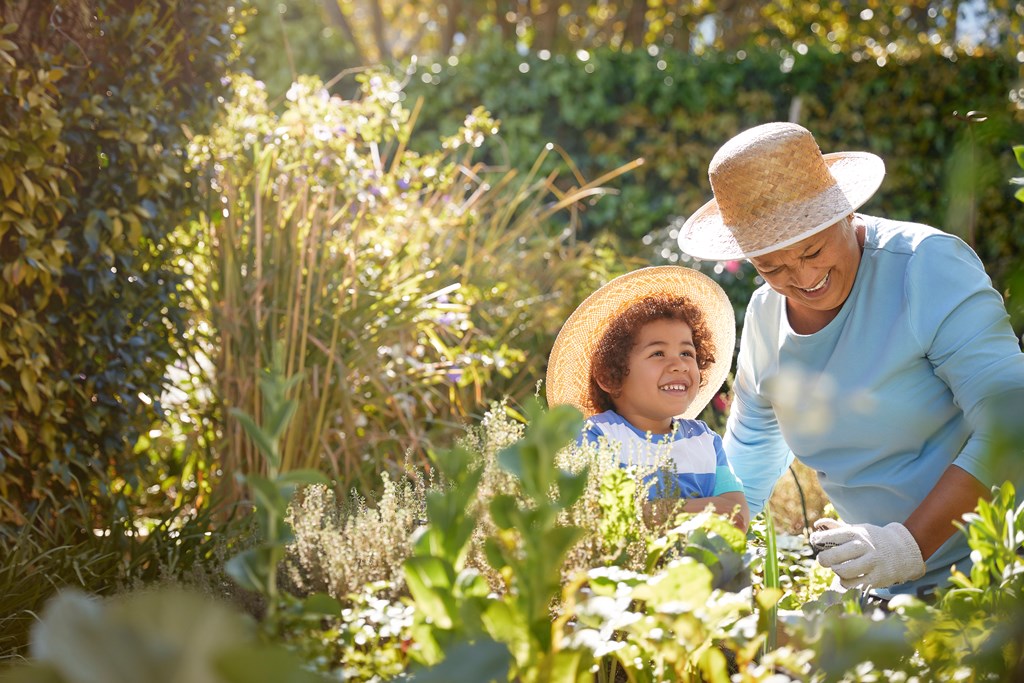 A grandmother and grandchild work together in a lush green garden.