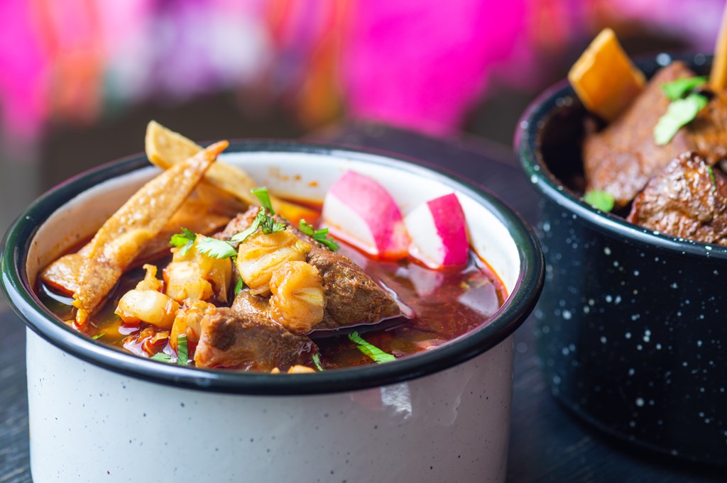 Mexican red pozole, hominy and pork stew, served with garnishes such as crispy tortillas, cilantro, lime and radish. Closeup.