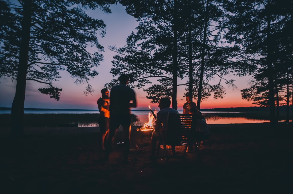 Group of young people gathered around a campfire by a lake.