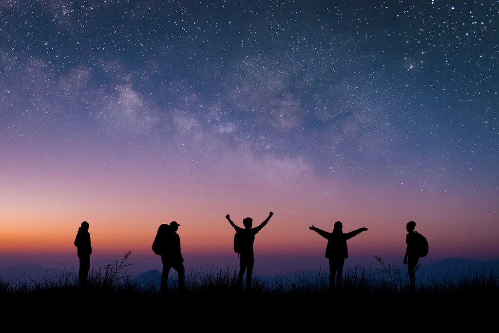 Silhouettes of five hikers at dusk with stars in the background.