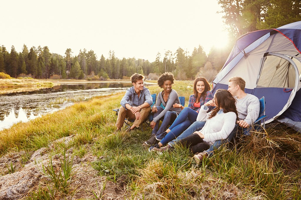 Friends on a camping trip relaxing by their tent near a lake