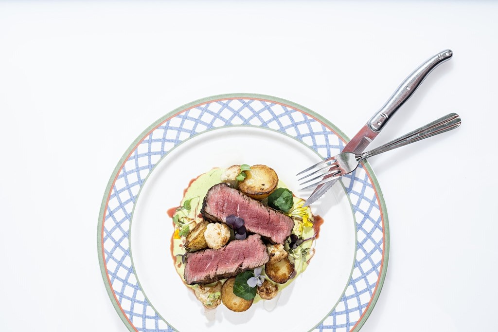 Plate of food with slices of steak on a white background.