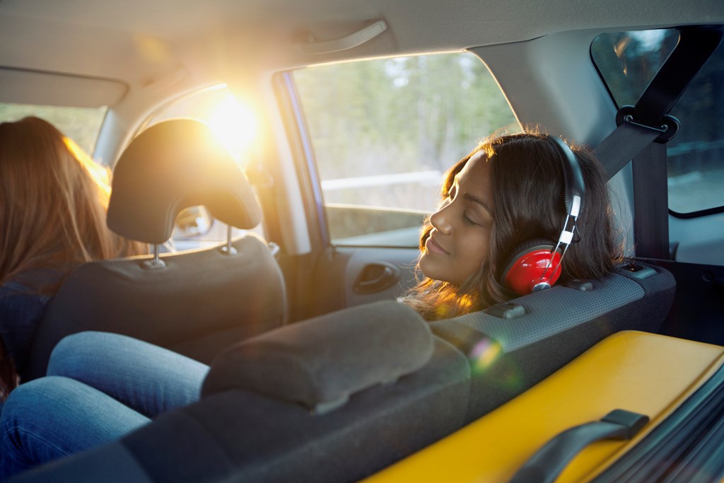 Young woman with headphones in the backseat of the car.
