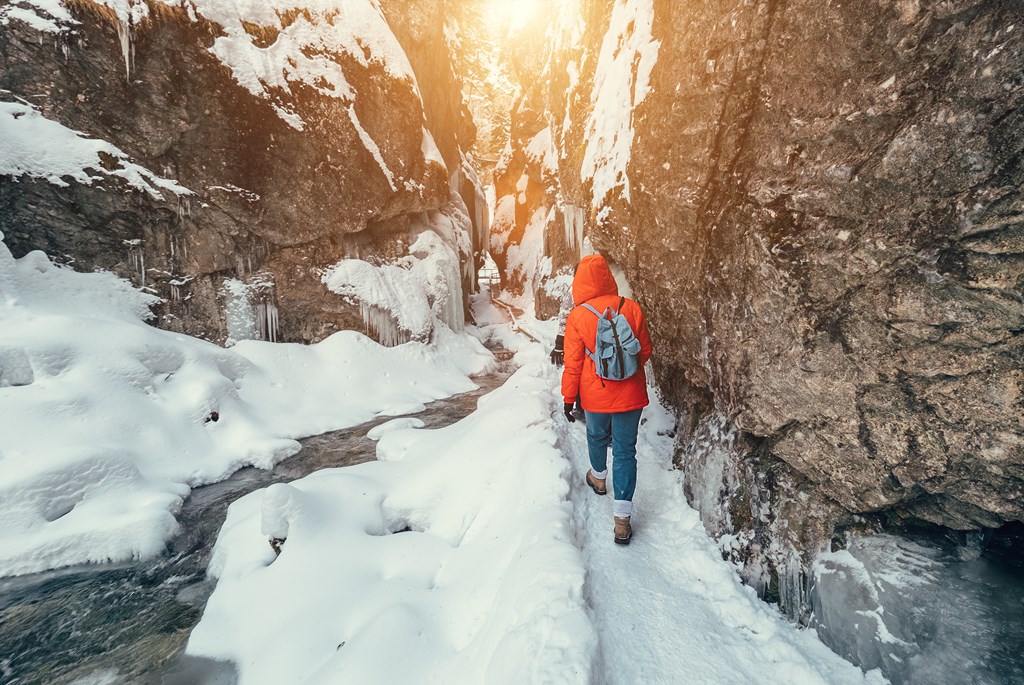 Hiker walks along a snow-covered trail along a stream.