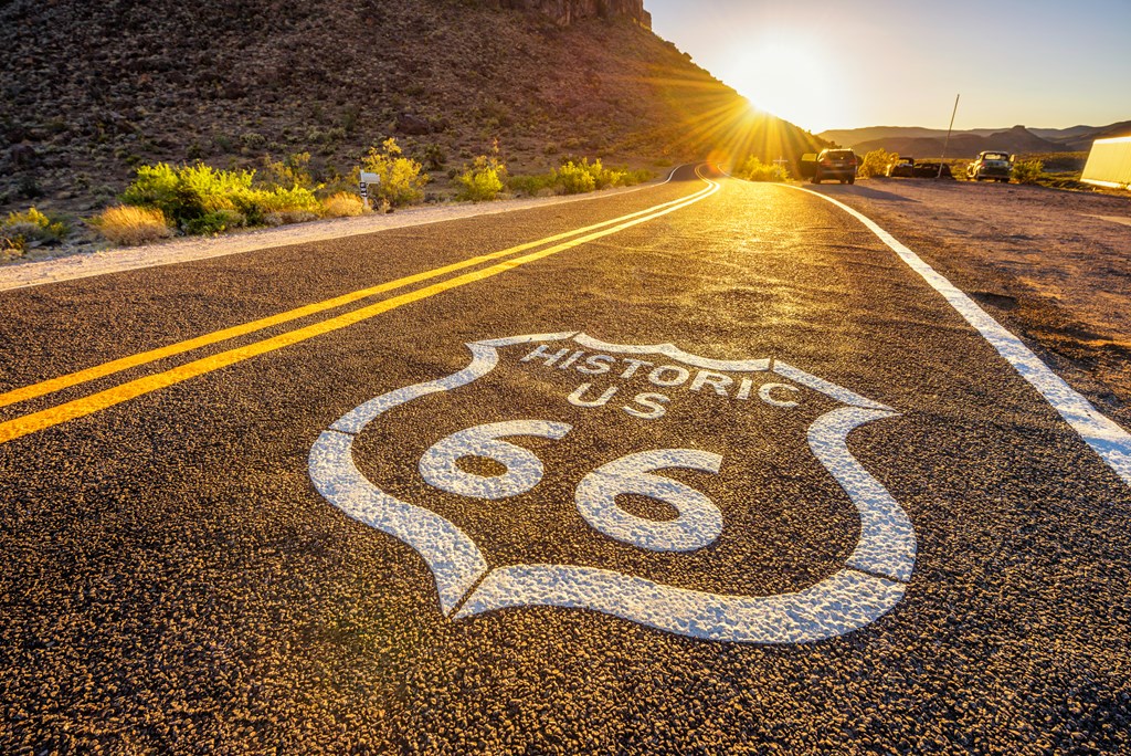 Street sign on historic route 66 in the Mojave desert photographed against the sun at sunset.