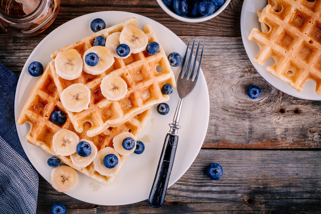 Fresh homemade waffles with blueberries and banana for breakfast on wooden background.