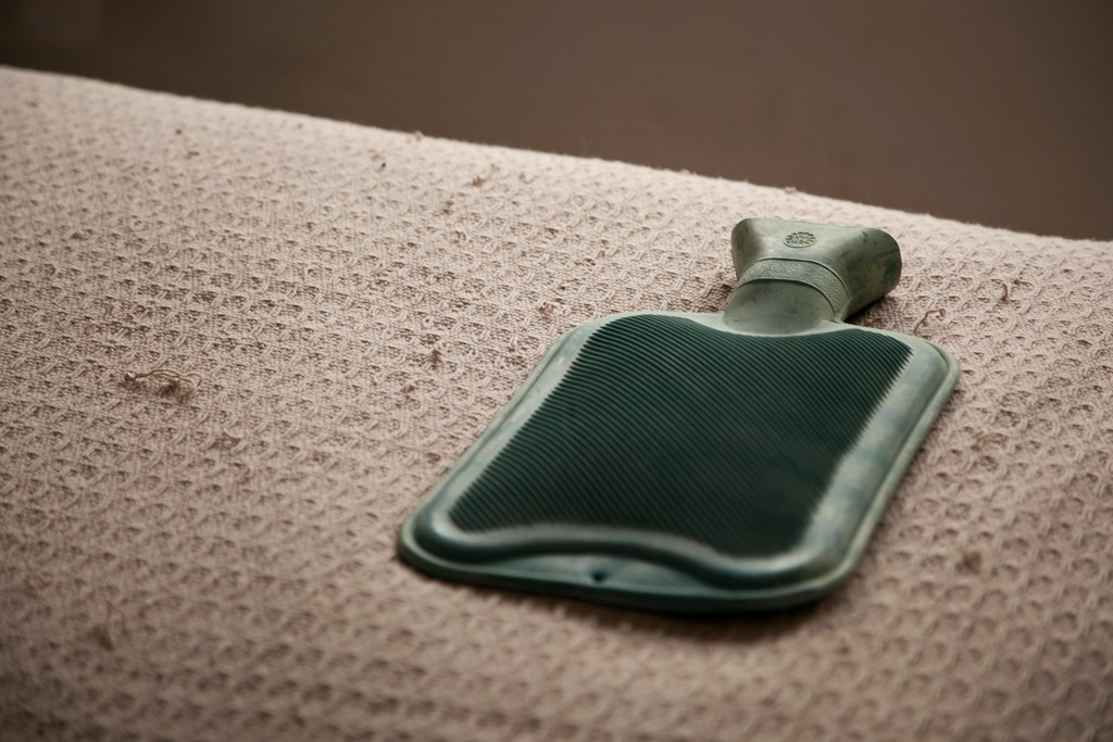 Green hot water bottle laying on a cream-colored blanket.