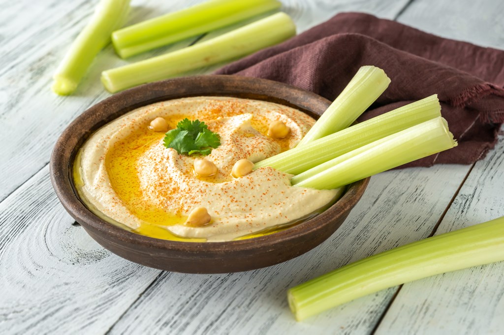 Bowl of hummus garnished with olive oil and paprika with sticks of celery on the side.