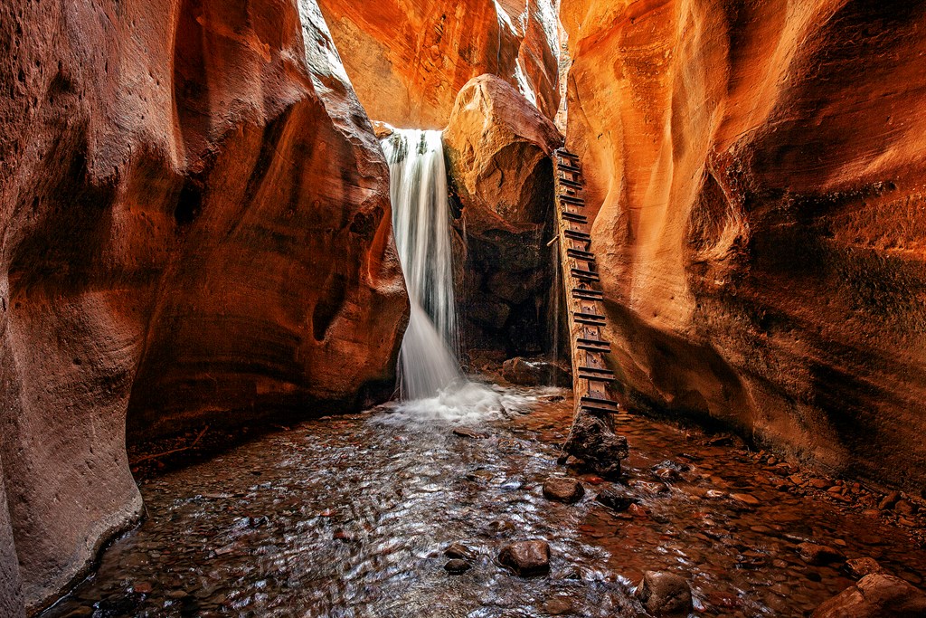 An image of Kanarra Falls as it tumbles over red rocks in a narrow canyon.