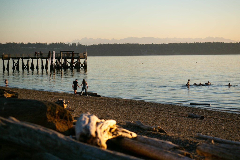 A sunset view of people walking along the sand at Kayak Point Beach.