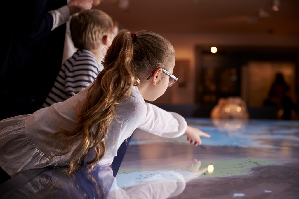 Young girl points at an interactive map in a museum.