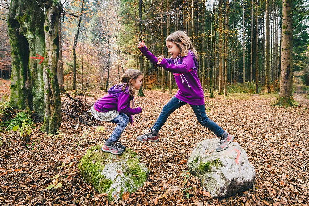 Identical twins are jumping from rocks in forest on hiking. 